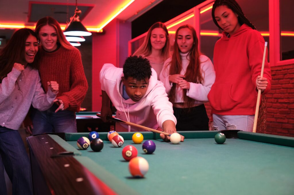 Young man playing pool with friends cheering in nightclub